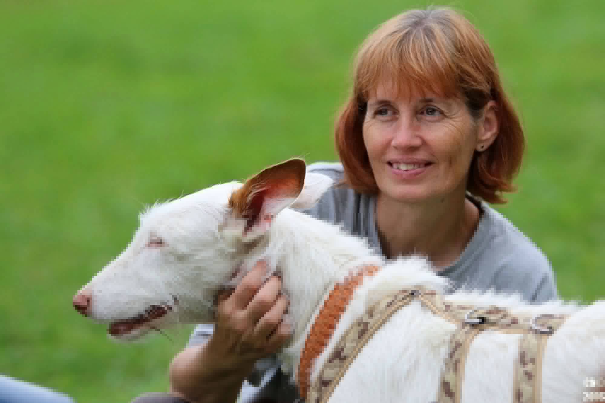 Christine Müller mit ihrem weissen Hund Abby auf einer grünen Wiese